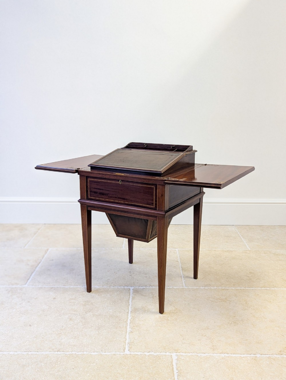 An Edwardian mahogany metamorphic writing table featuring opened side leaves, an angled leather inset writing slope, and tapered legs with line inlay.