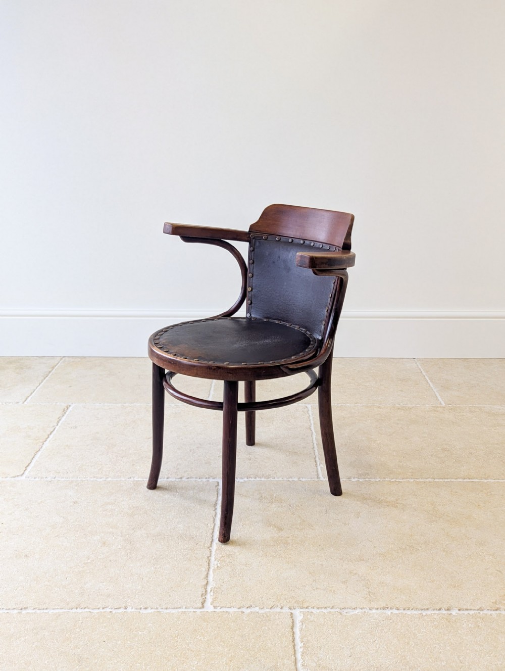 An Edwardian dark brown bentwood desk chair featuring curved wooden armrests and a dark leather upholstered seat and backrest with brass stud detailing.