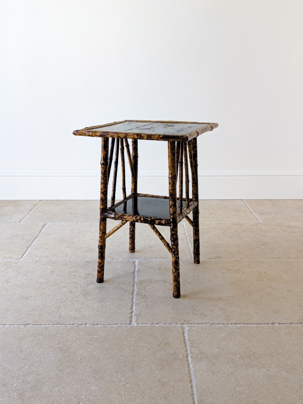 A late 19th-century square bamboo occasional table featuring a dark lacquered top, a lower tier shelf, and a mottled tortoiseshell finish.
