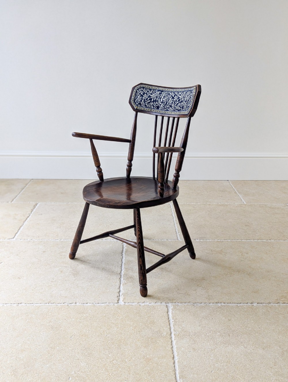 A dark stained elm and beech Windsor armchair featuring turned legs, a shaped saddle seat, spindle back, and a patterned foliate crest rail.