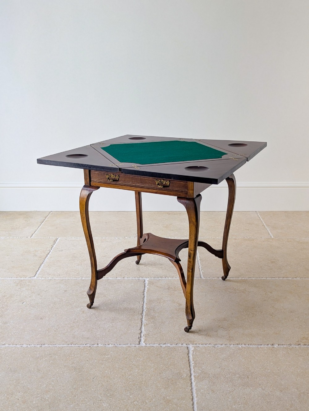 An Edwardian mahogany envelope card table with open triangular leaves revealing a green baize top, cabriole legs, and brass castors.