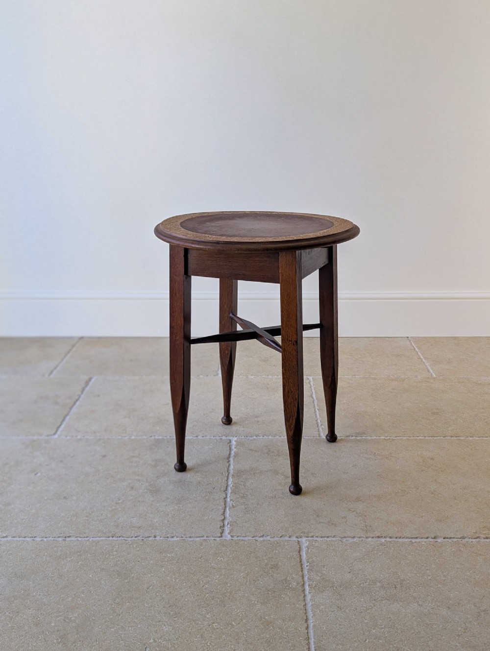 An Edwardian dark oak circular occasional table featuring four tapered legs joined by an X-frame cross stretcher.