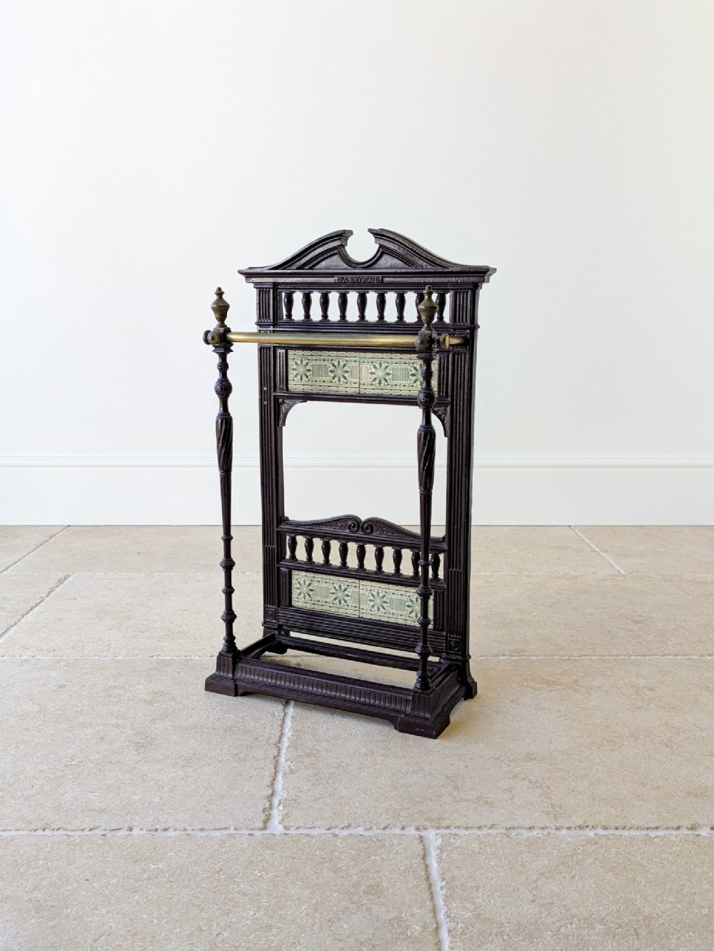 An Edwardian cast iron stick stand featuring decorative ceramic tiles, turned spindles, and a brass front rail.