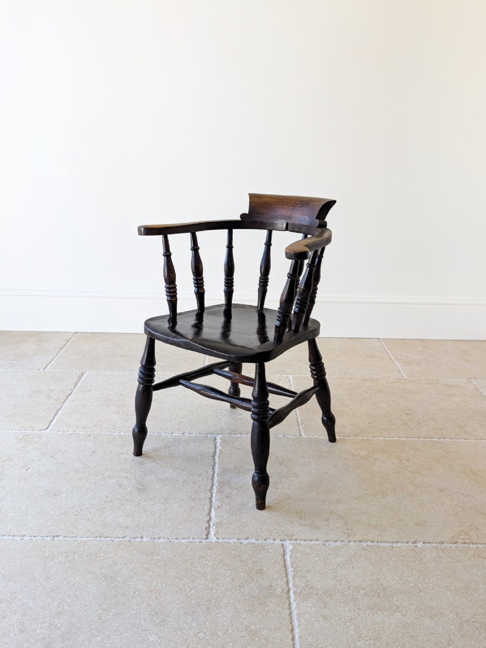 A dark-stained Victorian elm and ash captains chair featuring a curved crest, turned vertical spindles, a contoured seat, and turned legs joined by an H-stretcher.