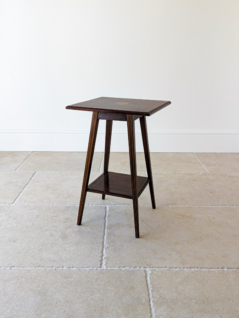 An Edwardian dark mahogany occasional table featuring a square top with satinwood line inlay, splayed legs, and a square lower shelf.