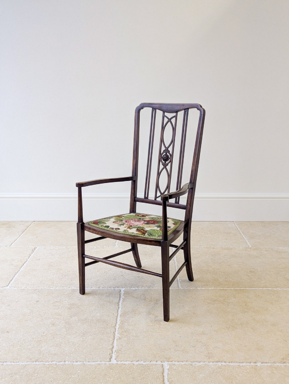 An Edwardian mahogany elbow chair with an inlaid pierced back splat, swept arms, and a floral needlepoint seat.