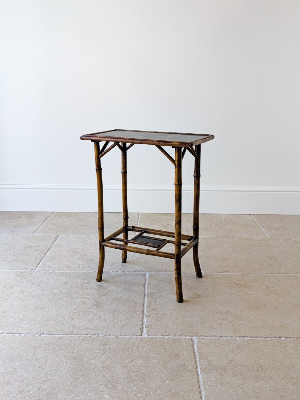 A late Victorian bamboo occasional table with a rectangular dark lacquered top surface, angled corner supports, and a lower tier shelf.