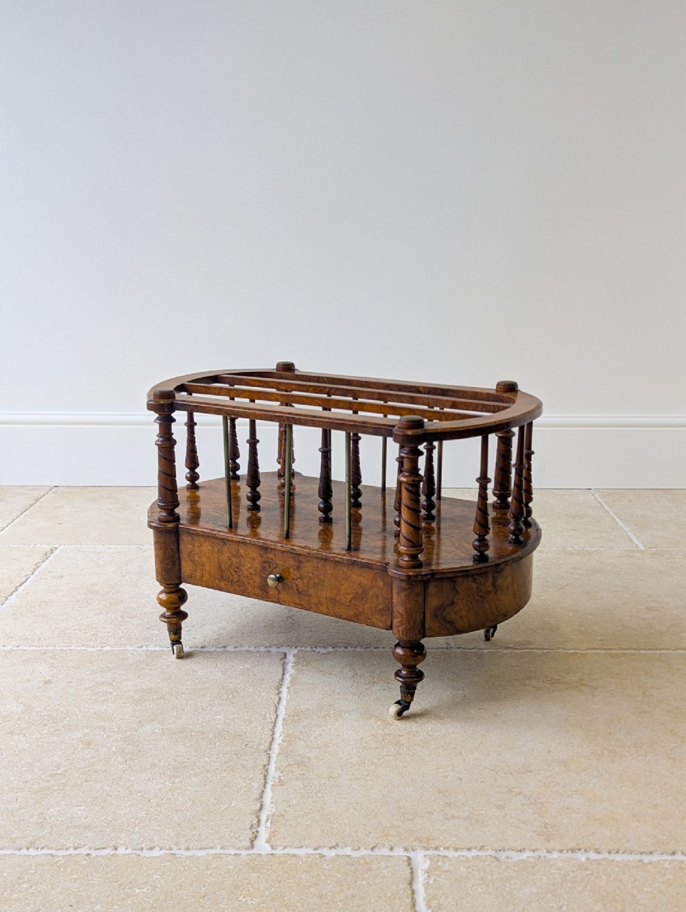 A Victorian burr walnut Canterbury featuring turned barley-twist spindles, brass support rails, a lower single drawer, and small castors.