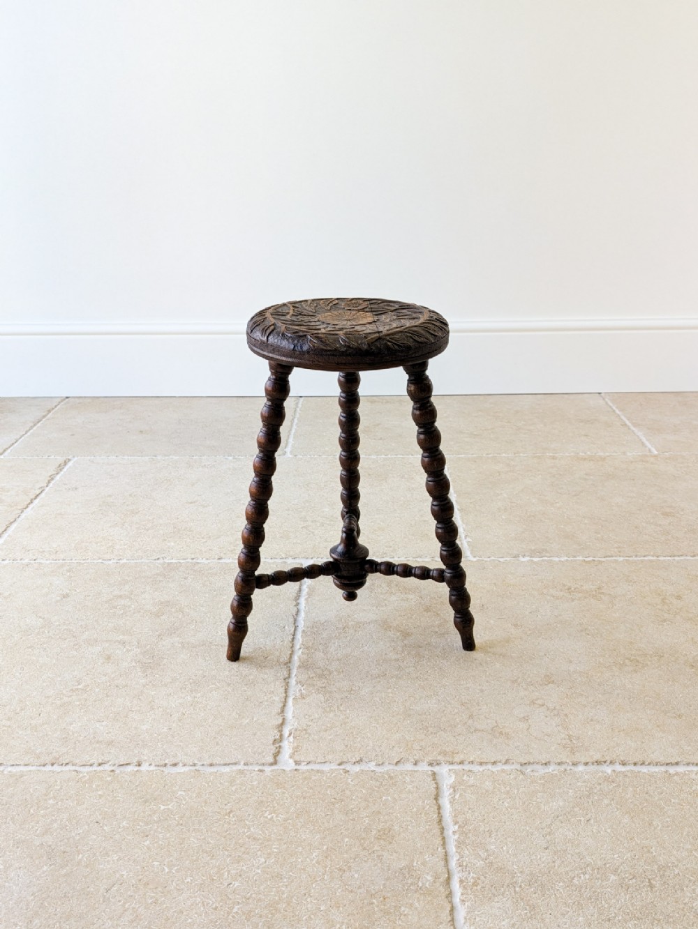 A late nineteenth-century Victorian dark oak tripod stool featuring a circular carved seat top and three bobbin-turned legs with a matching central stretcher.