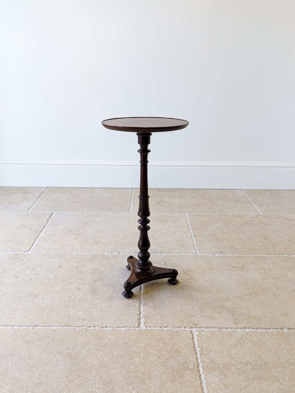 An antique Regency mahogany wine table featuring a circular dish top, a slender turned column, and a triform plinth base.
