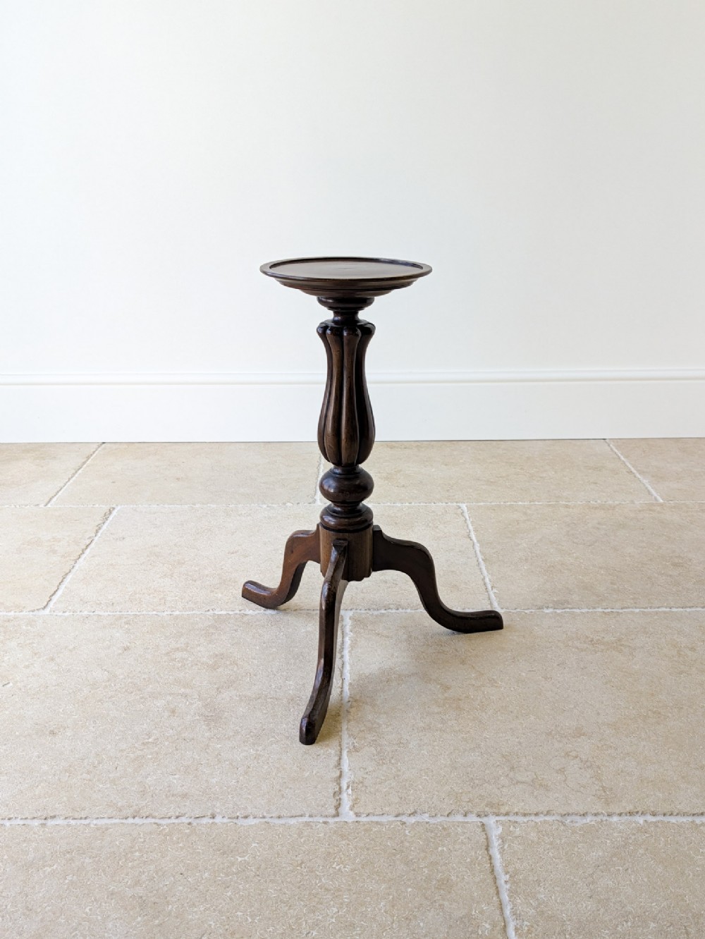 A late Victorian dark mahogany candle stand featuring a dished circular top supported by a carved fluted central column and three out-swept legs.