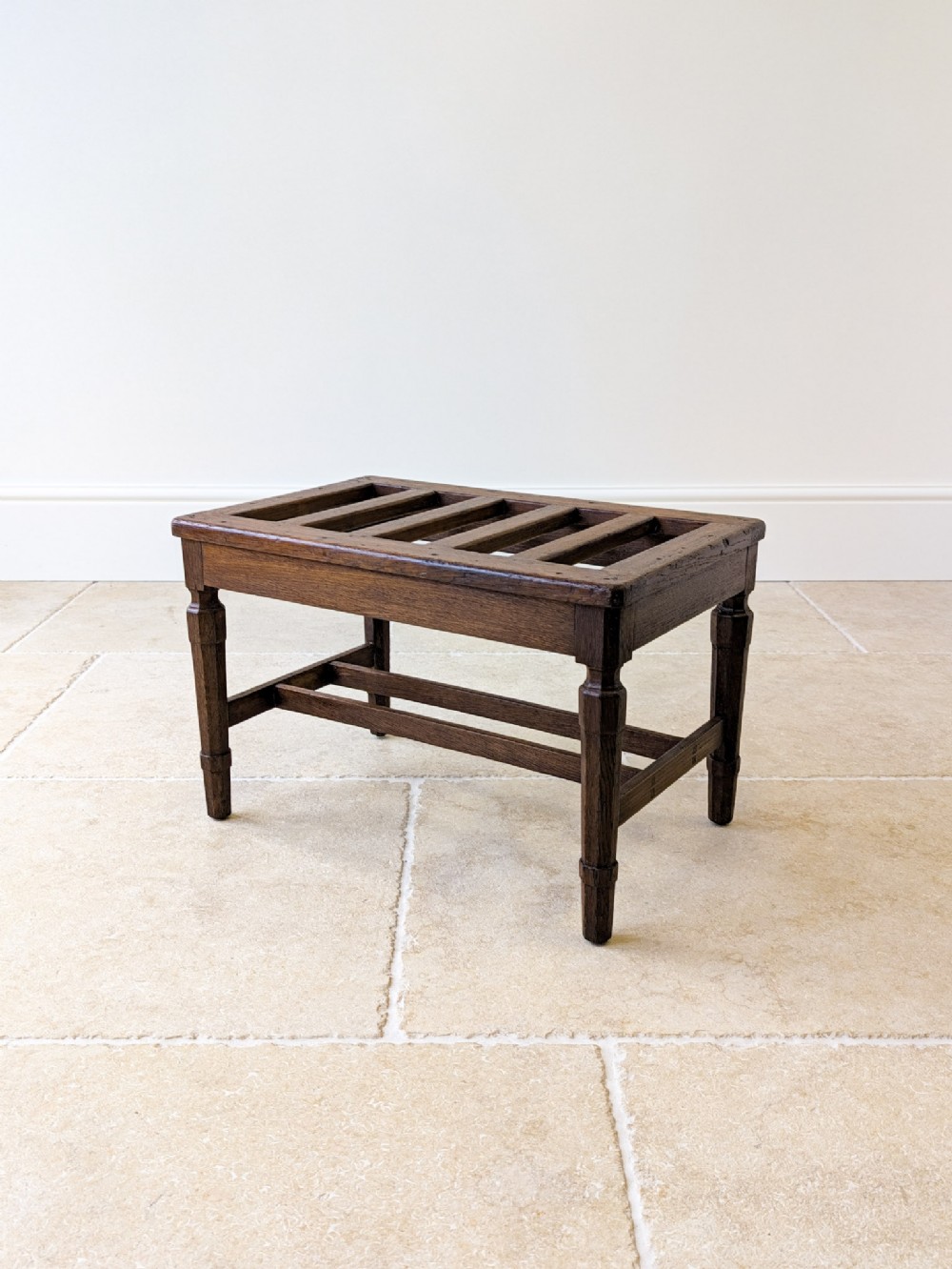 A dark oak Victorian luggage stand featuring a slatted top surface, turned legs, and lower cross-stretchers.