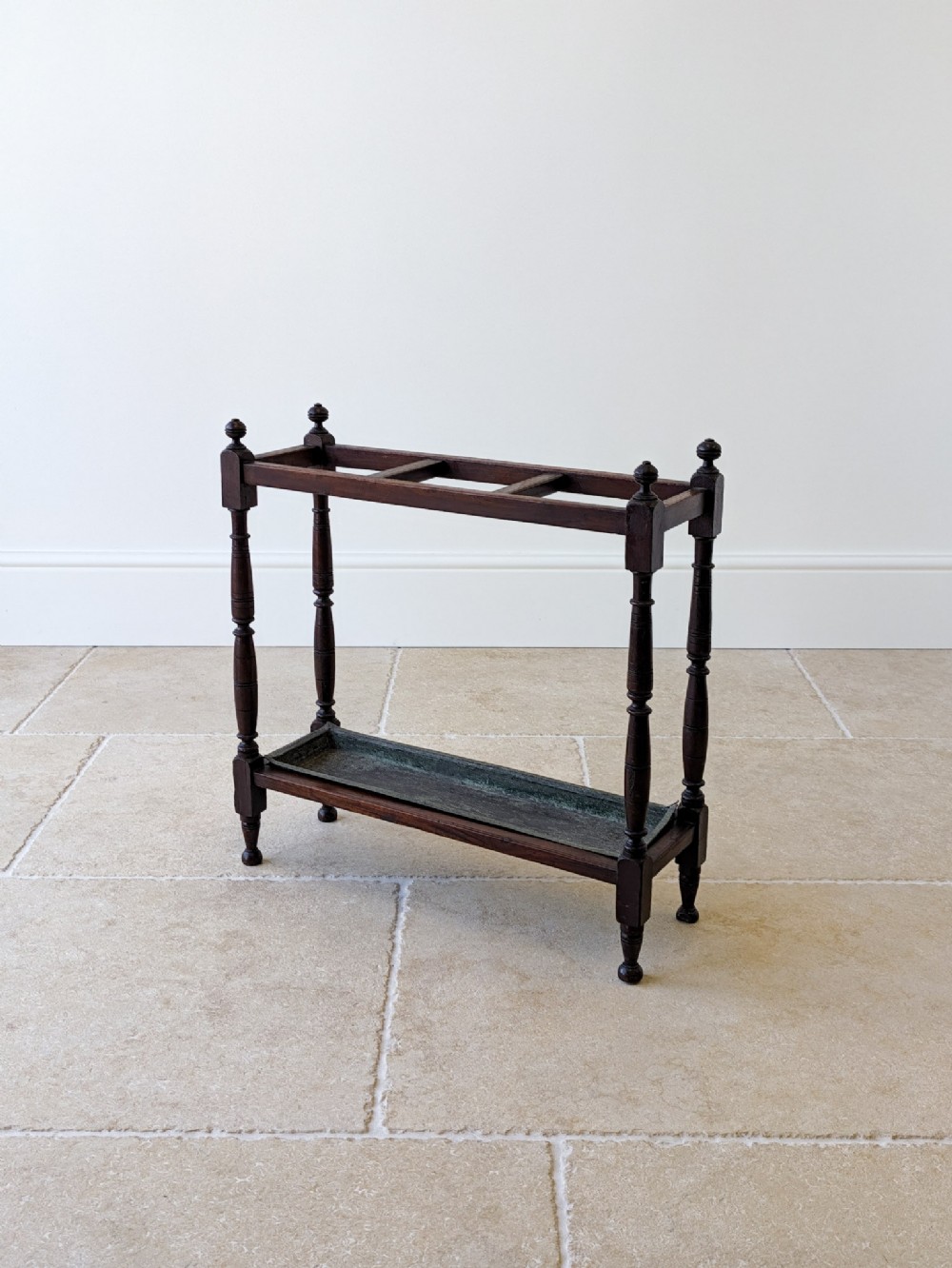 A Victorian dark mahogany wooden stick stand featuring turned supports, corner finials, top dividers, and a metal drip tray base.
