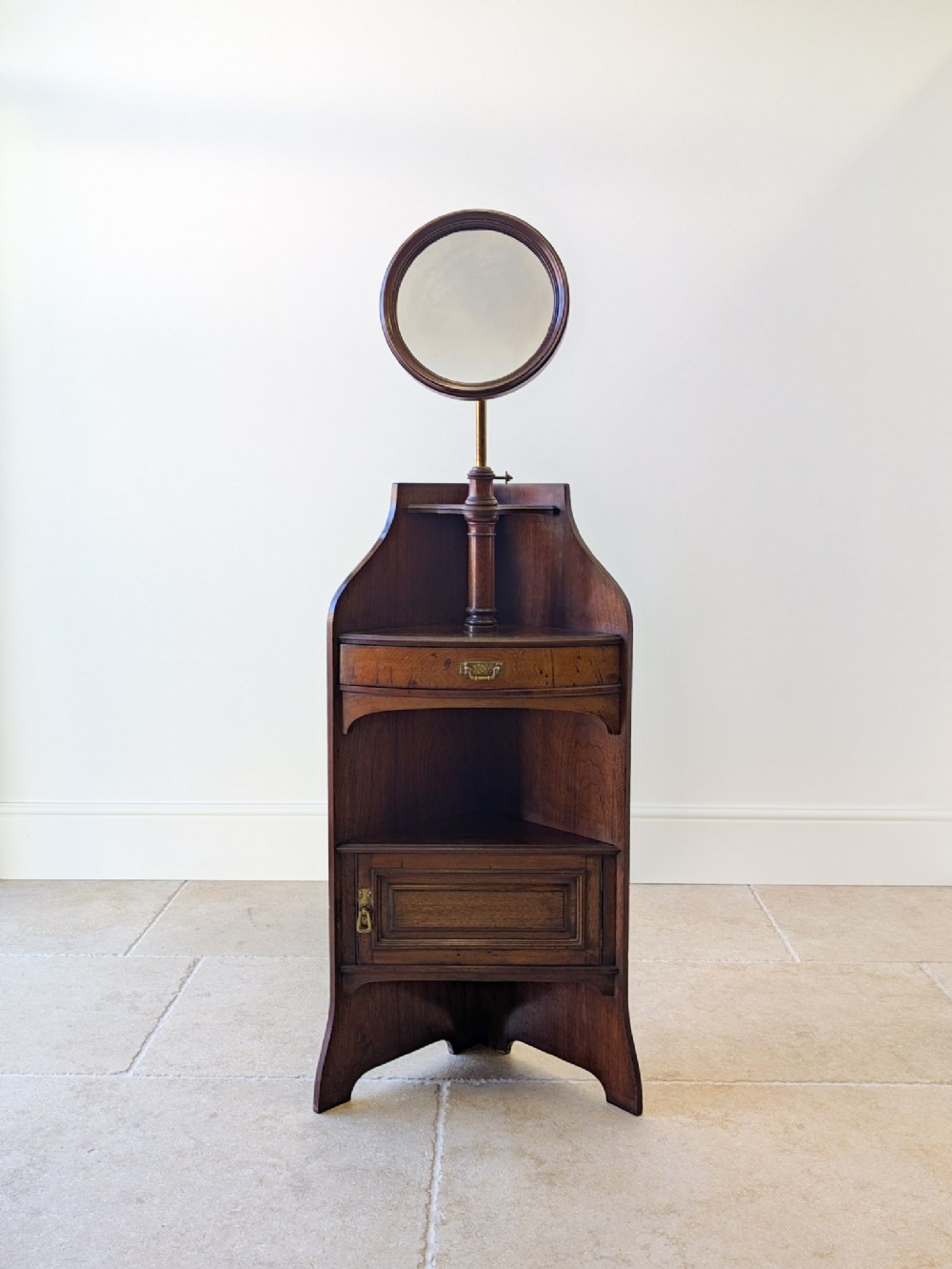 A late Victorian dark mahogany corner shaving stand featuring an adjustable circular mirror above a small shelf, drawer, and panelled lower cupboard.