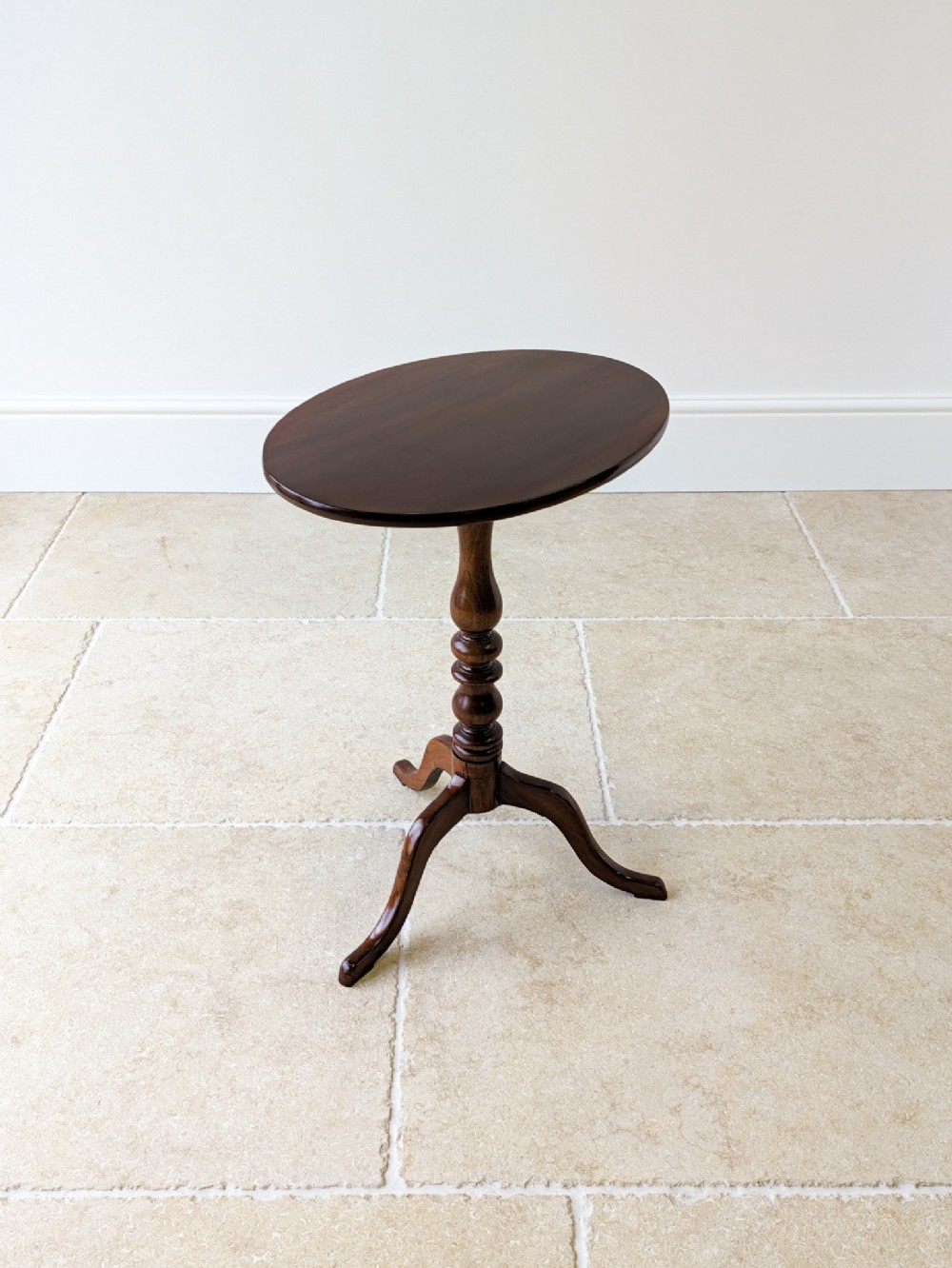 An antique Georgian mahogany tilt-top wine table featuring an oval top, turned central column, and a three-legged tripod base.
