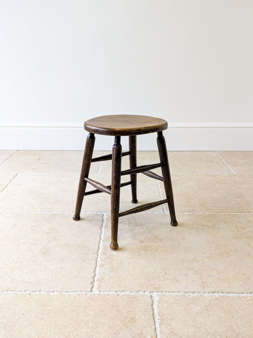 A late 19th-century country stool featuring a circular elm seat supported by four turned beech legs joined by spindle stretchers.