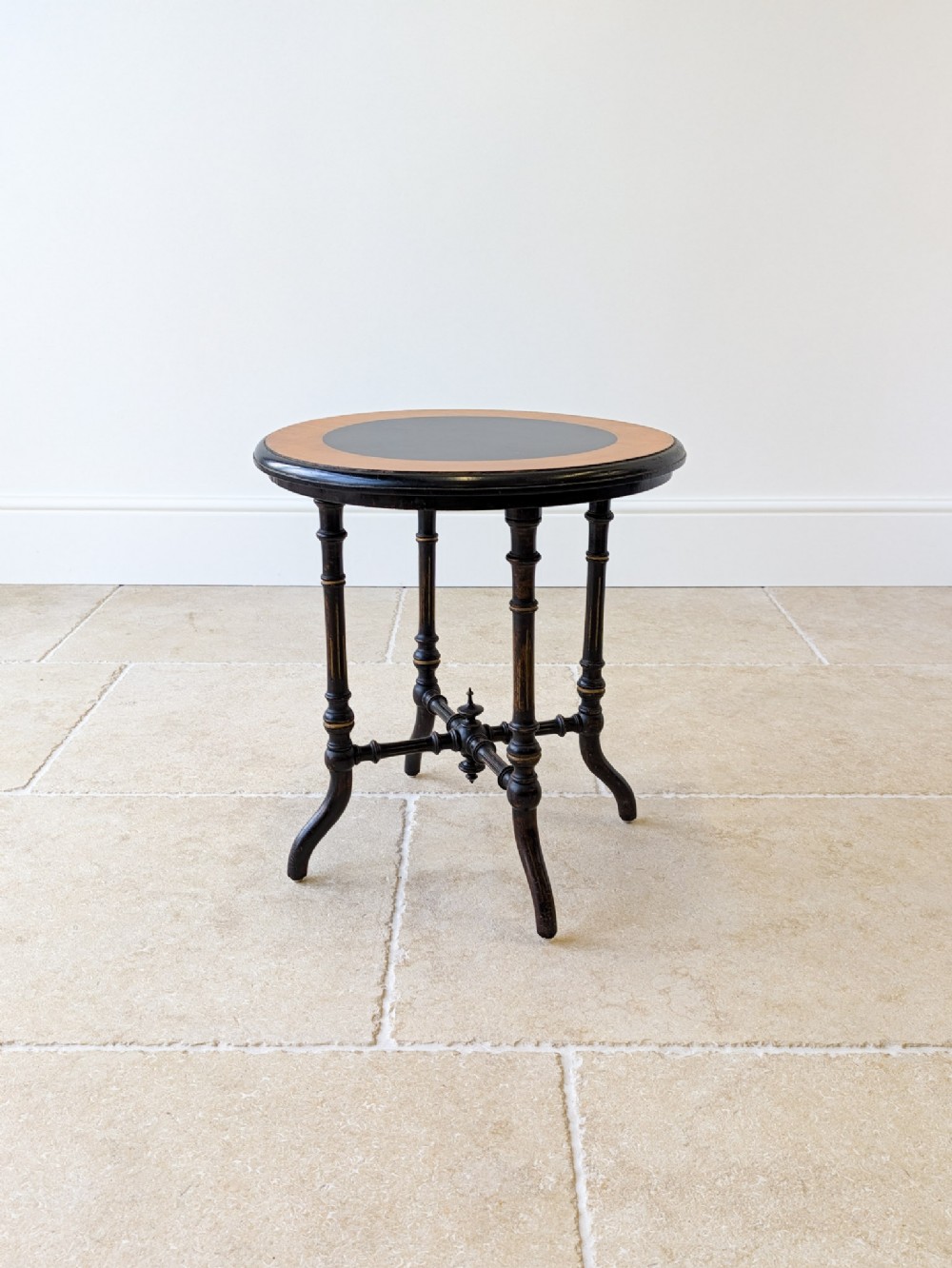 A Victorian Aesthetic Movement circular occasional table featuring an ebonised finish with turned legs, gilt highlights, and a central cross-stretcher.
