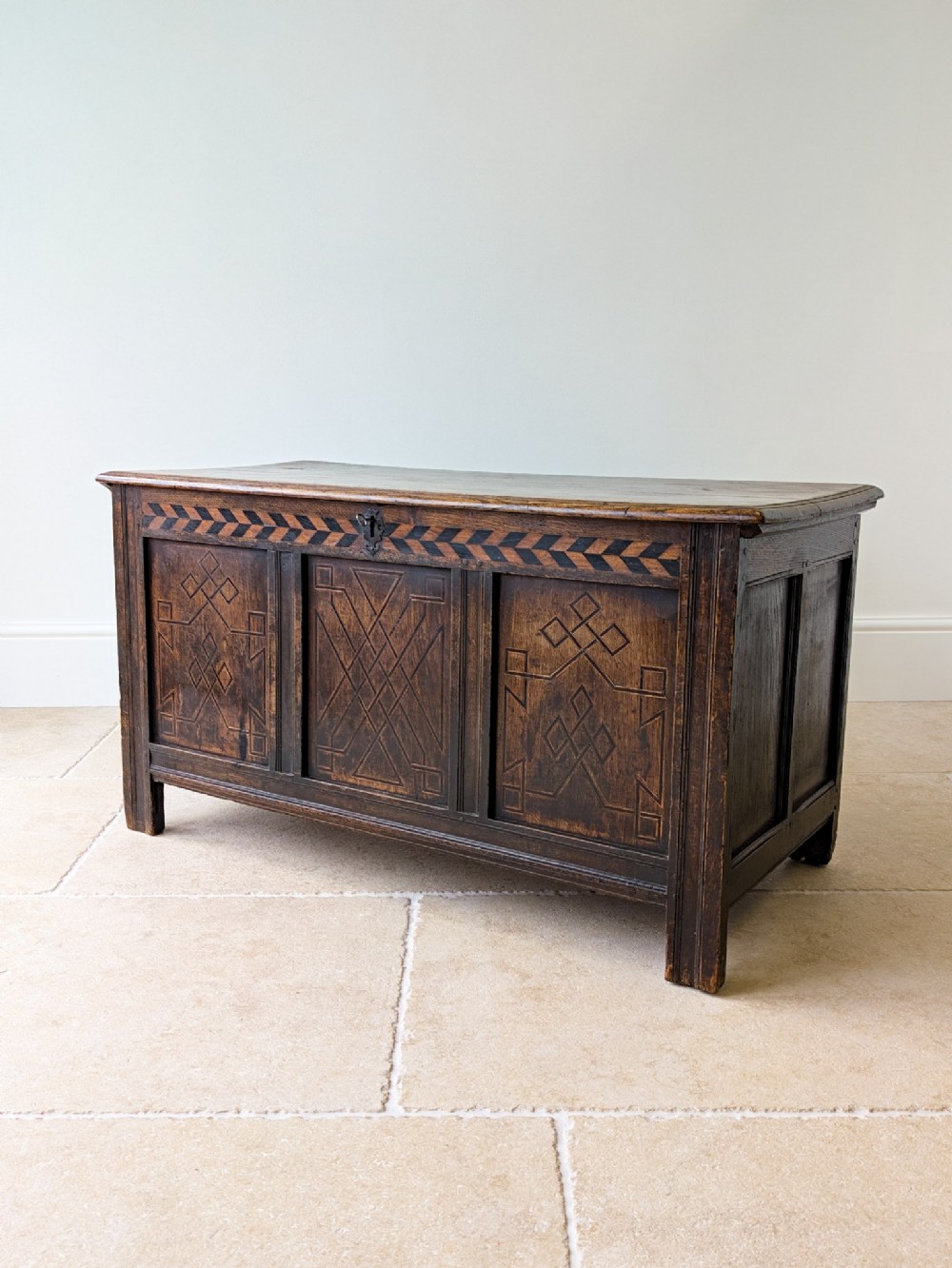 A 17th-century Charles II dark oak coffer featuring a geometric inlaid frieze and three carved geometric front panels.