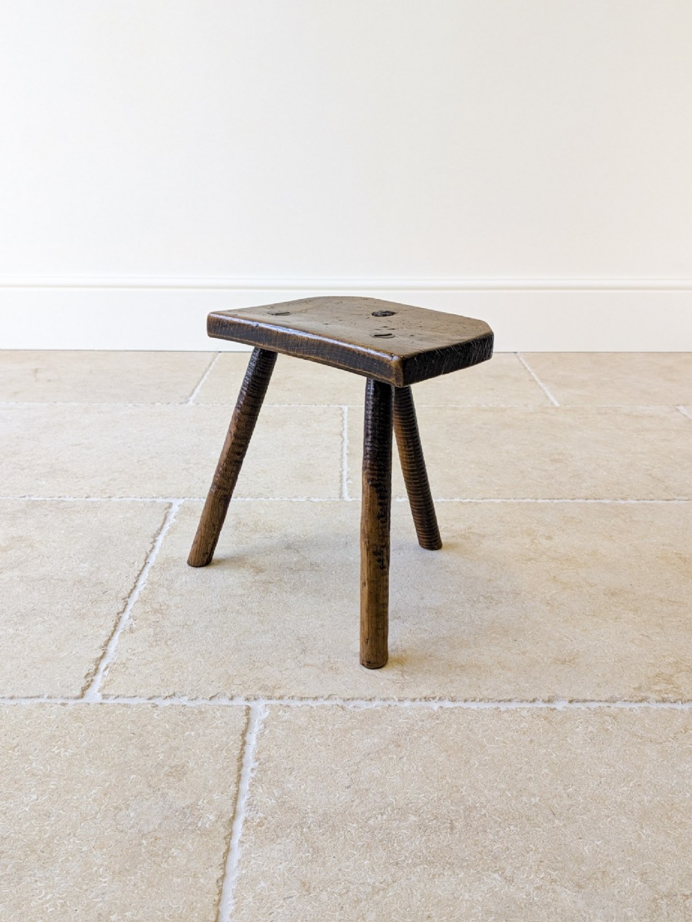 A rustic nineteenth-century dark wood three-legged stool with a contoured elm seat and turned ash splayed legs.