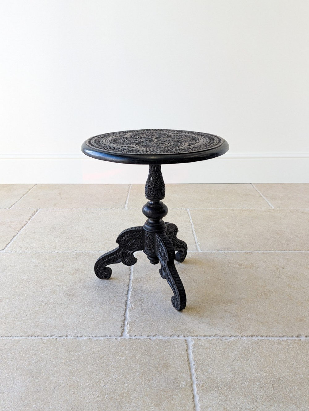 An antique Victorian ebonised wooden occasional table with an intricately hand-carved circular top, a turned central stem, and a carved tripod base.