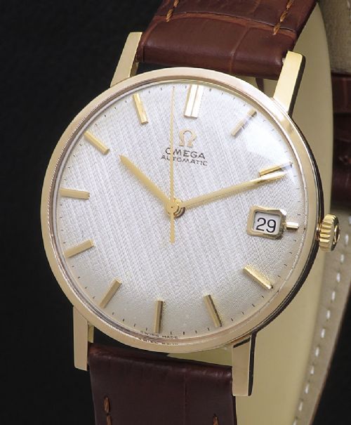fig 2. A 1965 solid 9ct gold Omega automatic wristwatch featuring a textured silver dial, gold baton hour markers, and a brown leather strap.