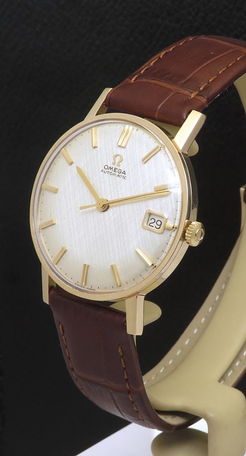 fig 3. A 1965 solid 9ct gold Omega automatic wristwatch featuring a textured silver dial, gold baton hour markers, and a brown leather strap.