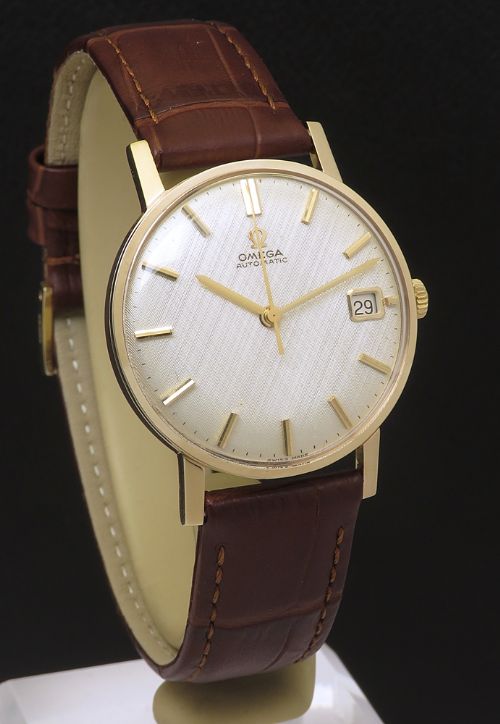 fig 4. A 1965 solid 9ct gold Omega automatic wristwatch featuring a textured silver dial, gold baton hour markers, and a brown leather strap.