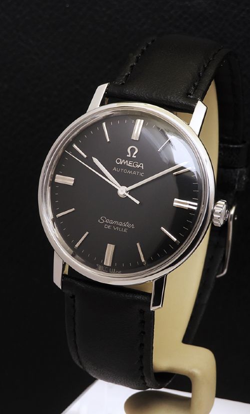 fig 1. A vintage Omega Seamaster DeVille wristwatch featuring a round stainless steel case, a black dial with silver baton hour markers, and a stitched black leather strap.