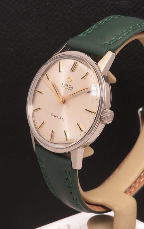 fig 2. A 1967 stainless steel Omega Seamaster Automatic wristwatch with a silver dial, gold baton hour markers, and a dark green leather strap.