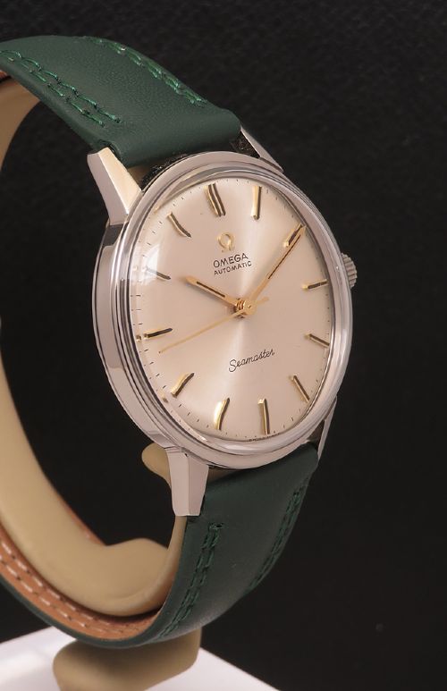 fig 4. A 1967 stainless steel Omega Seamaster Automatic wristwatch with a silver dial, gold baton hour markers, and a dark green leather strap.