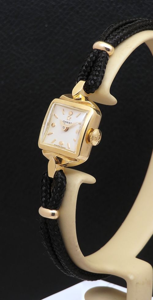 fig 2. An 18ct yellow gold 1956 Omega ladies cocktail watch featuring a square white dial and black braided cord strap.