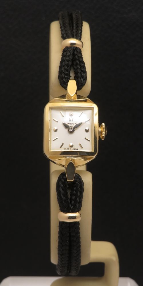 fig 3. An 18ct yellow gold 1956 Omega ladies cocktail watch featuring a square white dial and black braided cord strap.