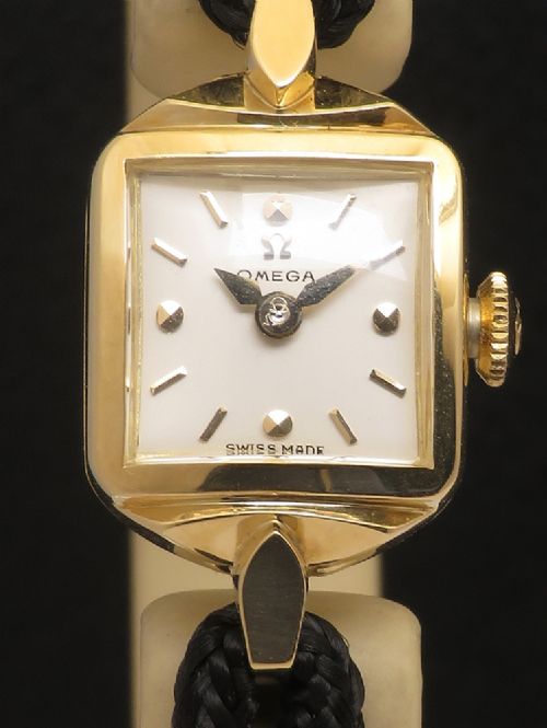 fig 4. An 18ct yellow gold 1956 Omega ladies cocktail watch featuring a square white dial and black braided cord strap.
