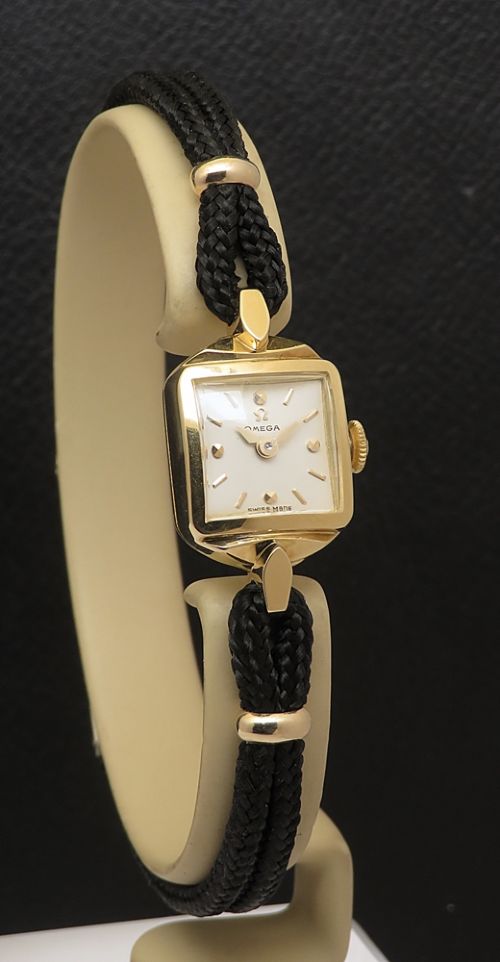 fig 5. An 18ct yellow gold 1956 Omega ladies cocktail watch featuring a square white dial and black braided cord strap.