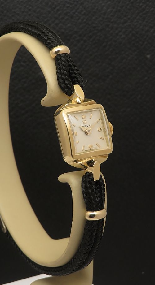 An 18ct yellow gold 1956 Omega ladies cocktail watch featuring a square white dial and black braided cord strap. View VII