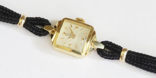 An 18ct yellow gold 1956 Omega ladies cocktail watch featuring a square white dial and black braided cord strap. View X
