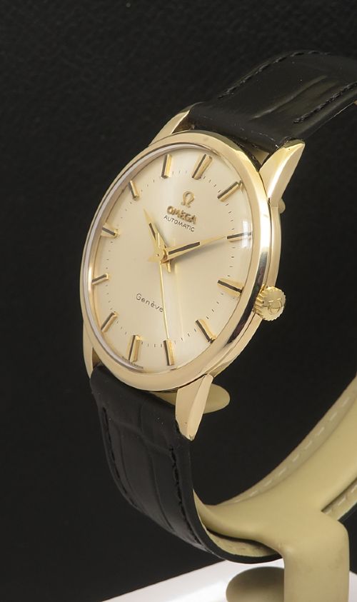 fig 2. A 1967 Omega Geneve automatic wristwatch featuring a circular solid 9ct gold case, a silvered sunburst dial with gold baton hour markers, and a black leather strap.