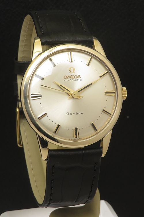 fig 3. A 1967 Omega Geneve automatic wristwatch featuring a circular solid 9ct gold case, a silvered sunburst dial with gold baton hour markers, and a black leather strap.