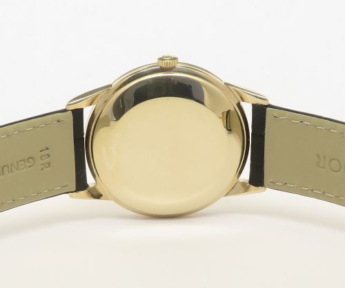 A 1967 Omega Geneve automatic wristwatch featuring a circular solid 9ct gold case, a silvered sunburst dial with gold baton hour markers, and a black leather strap. View VII