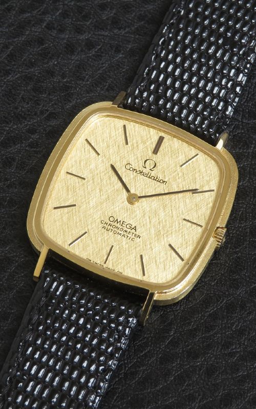 fig 1. A 1968 Omega Constellation Deluxe wristwatch featuring a cushion-shaped 18ct gold case, brushed champagne dial, baton indices, and a black textured leather strap.