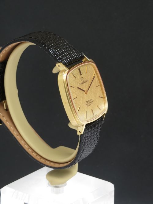 A 1968 Omega Constellation Deluxe wristwatch featuring a cushion-shaped 18ct gold case, brushed champagne dial, baton indices, and a black textured leather strap. View VII