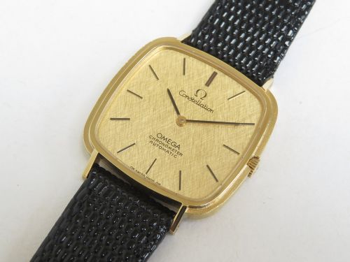 A 1968 Omega Constellation Deluxe wristwatch featuring a cushion-shaped 18ct gold case, brushed champagne dial, baton indices, and a black textured leather strap. View VIII