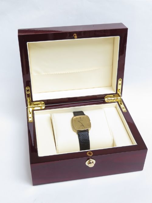 A 1968 Omega Constellation Deluxe wristwatch featuring a cushion-shaped 18ct gold case, brushed champagne dial, baton indices, and a black textured leather strap. View IX