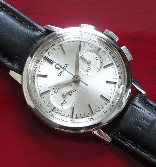 A 1963 stainless steel Omega chronograph wristwatch featuring a silver dial with two sub-dials and a black leather strap. View X