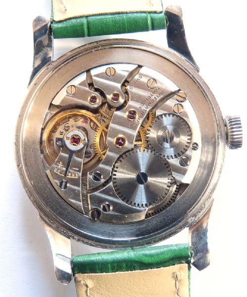 A vintage Swiss wristwatch featuring a stainless steel case, white dial with gold-tone markers, sub-seconds subdial, and a green leather strap. View VI