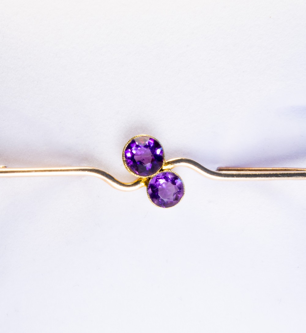 An early 20th century 9ct gold bar brooch featuring a central curved design set with two round-cut purple amethysts. View II