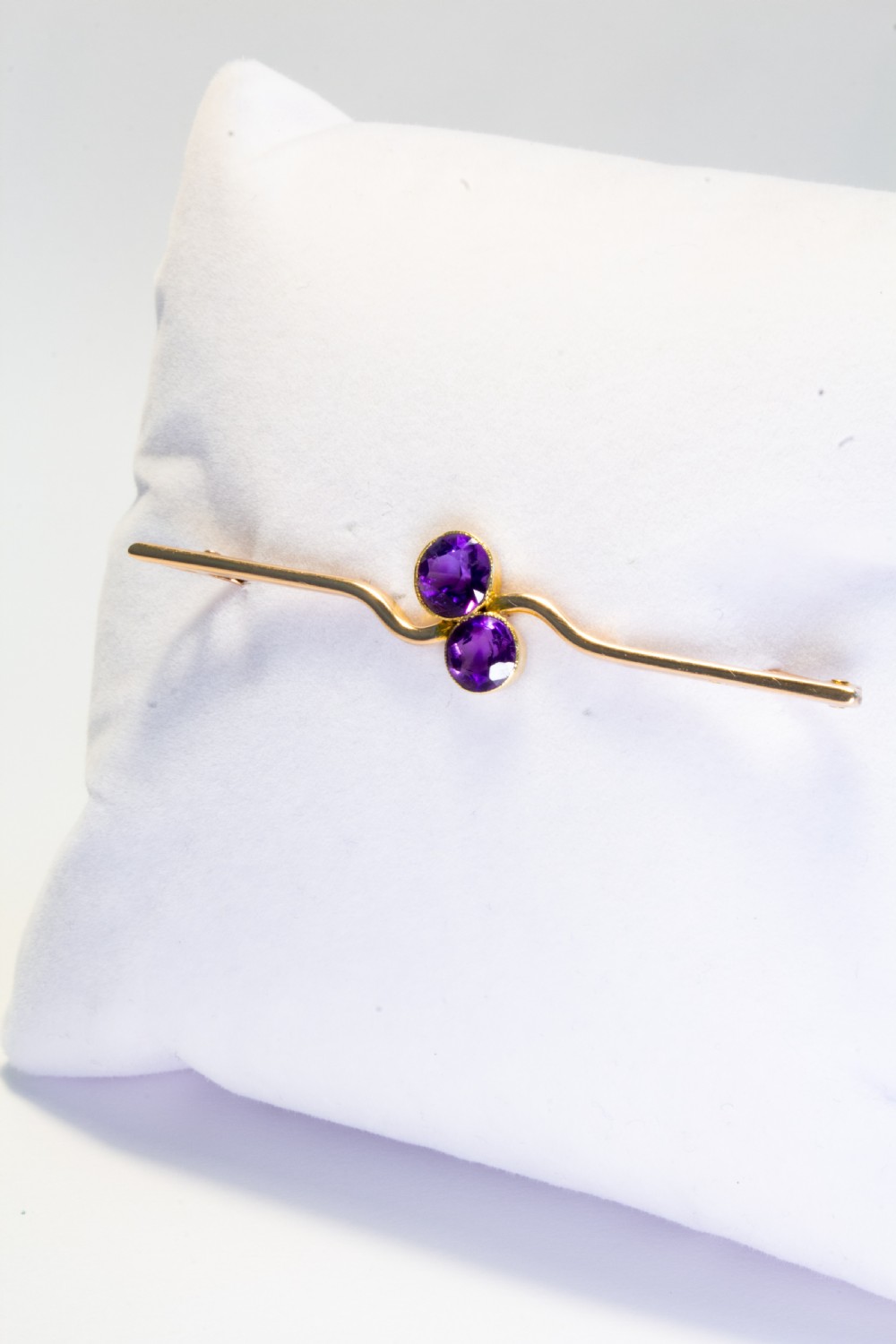 An early 20th century 9ct gold bar brooch featuring a central curved design set with two round-cut purple amethysts. View IV