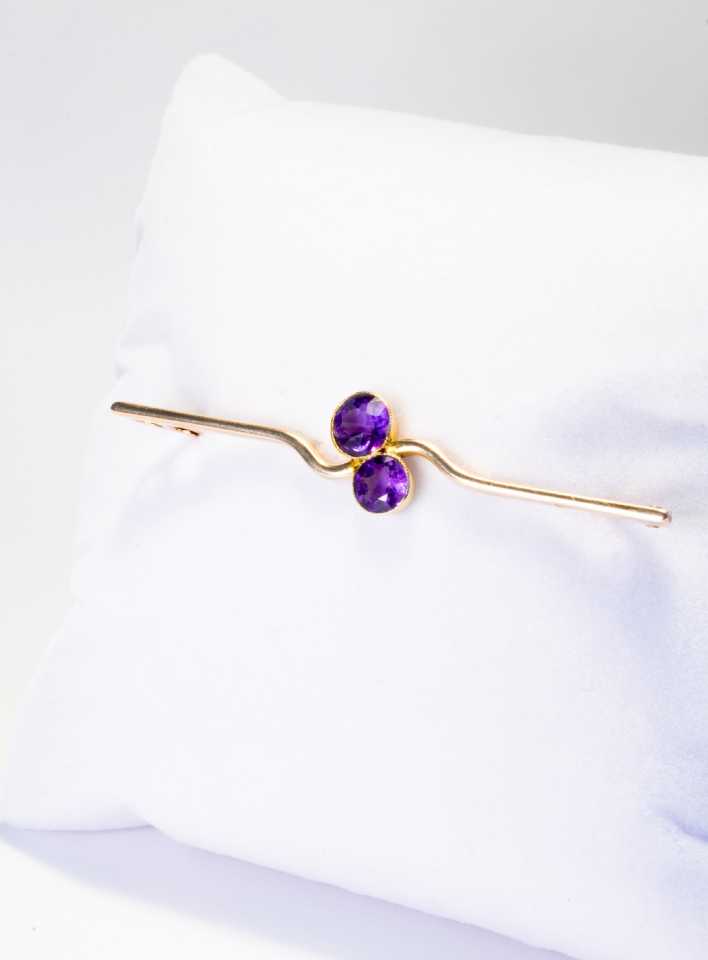 An early 20th century 9ct gold bar brooch featuring a central curved design set with two round-cut purple amethysts. View V