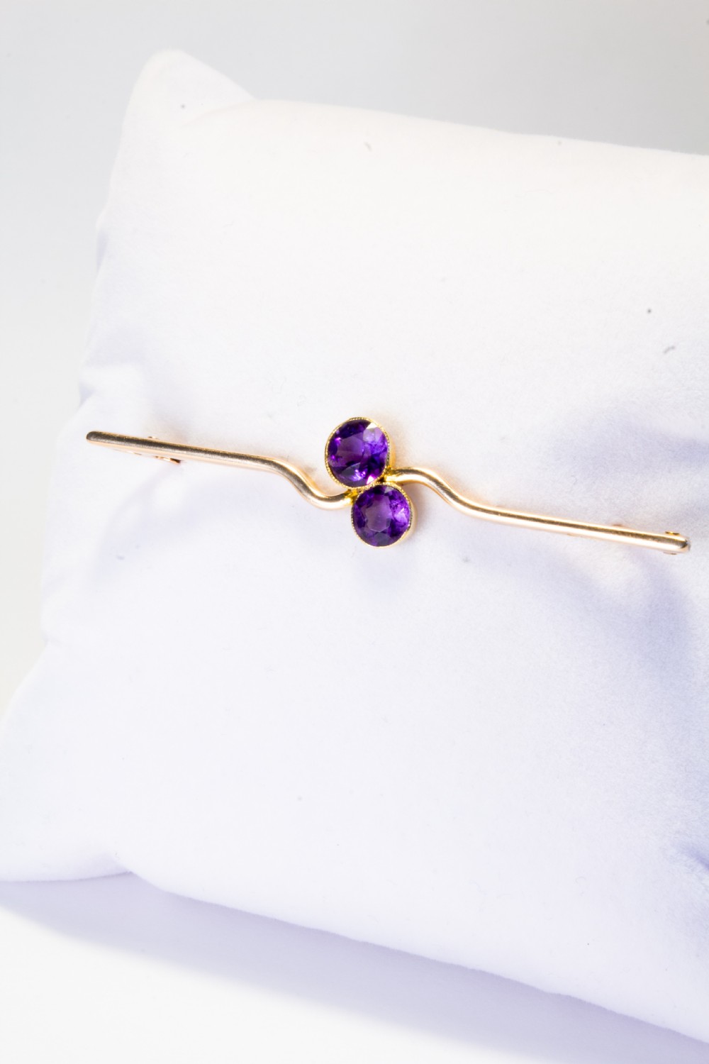 An early 20th century 9ct gold bar brooch featuring a central curved design set with two round-cut purple amethysts. View VI