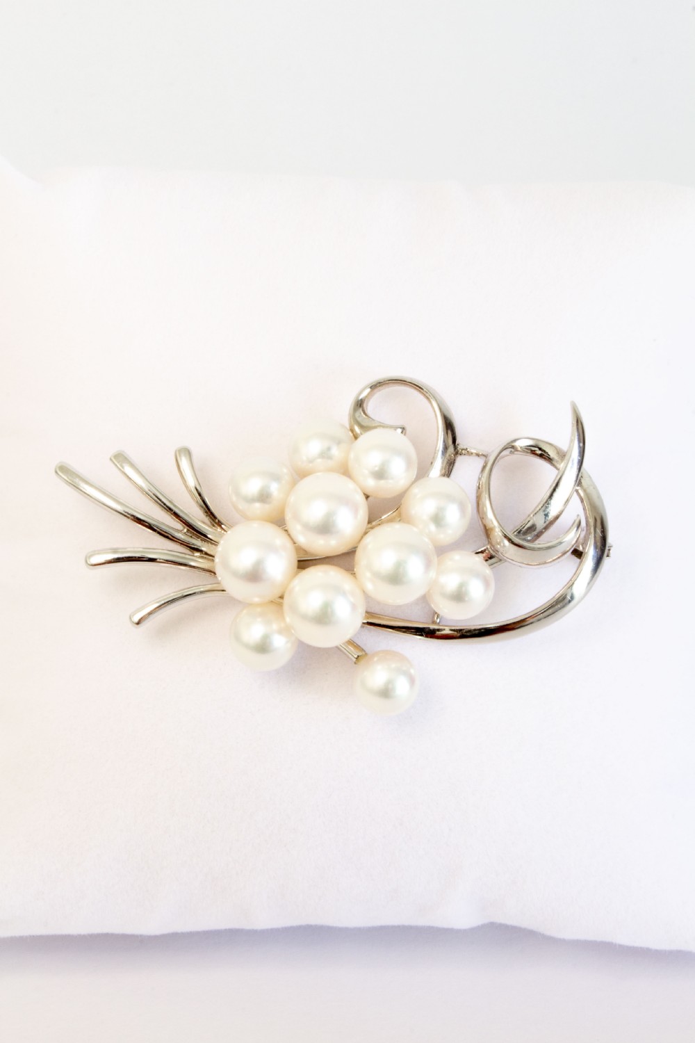 A sterling silver brooch featuring a cluster of round white cultured pearls framed by fluid, polished metal curves and ribbon flourishes. View V